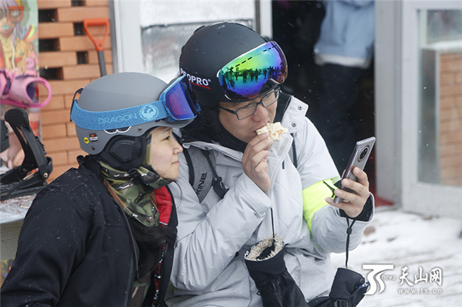 两位滑雪爱好者一边吃馕一欣赏着他们拍的照片。